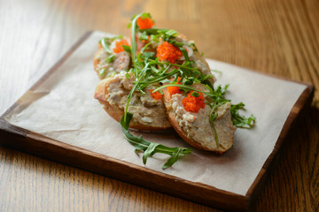 Italian bruschetta with salmon butter, capelin caviar, cherry tomatoes and parsley served on wooden cutting board
