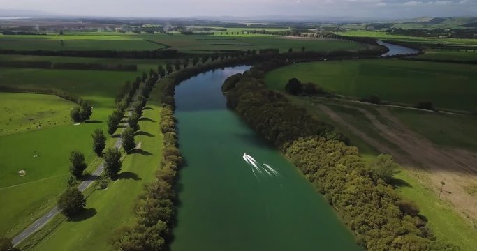 Drone shot of a river, boat and water ski rider.  White car going by on the road next to the river.
