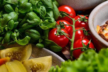 Large homegrown tomatoes surrounded by green tomatoes and spinach on a dark wooden table. Healthy eating food concept