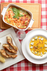 Traditional Italian cuisine, lasagna made with minced beef, pumpkin soup with seeds and cheese and fried fish. Top view.