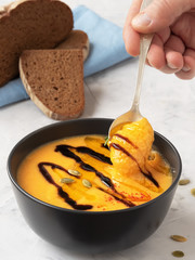 Pumpkin cream soup with balsamil souse and olive oil. Decorated rosemary branсh and pumpkin seeds. Traditional ingredients, healthy food concept. Blue napkin, gray stone background, close up