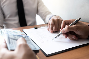 The businessman signed a contract agreement documents and receive a bribe from another businessman sitting in front at the office.