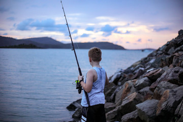 Young boy fishing off rocks at twilight
