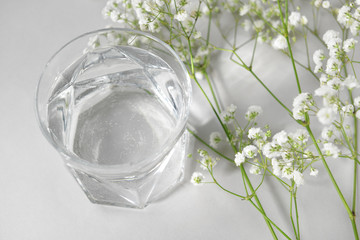 Glass of clean water and flowers on light background