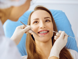 Smiling young woman with orthodontic brackets examined by dentist at dental clinic. Healthy teeth and medicine concept