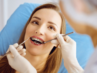 Smiling young woman with orthodontic brackets examined by dentist at dental clinic. Healthy teeth...