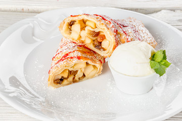 A piece of apple strudel on a white plate decorated with mint