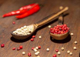 Two wooden spoons with red and white pepper on a wooden surface.