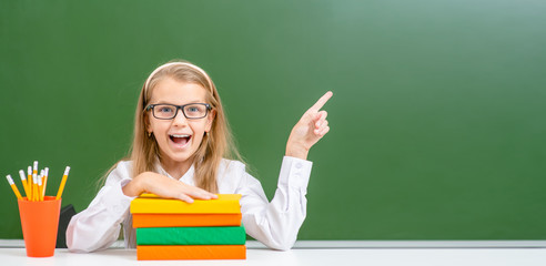 Surprised girl with books points on empty chalk board. Empty space for text