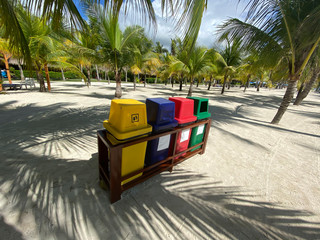 Colored containers for sorting garbage on a white sandy beach in a palm forest. Ecology, recycling.