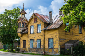 Fototapeta na wymiar Old wooden yellow house with small tower during sunny day in summer in Riga, Latvia. Traditional Latvian Wooden Architecture.