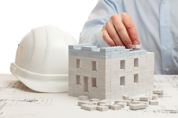 Hand of an architect constructing a house with toy blocks