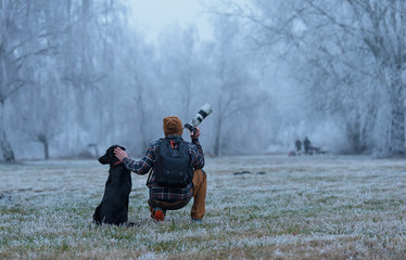 Photographer and his dog looking something in the winter park