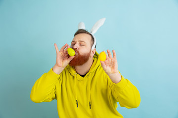 Egg hunt coming. Caucasian man as an Easter bunny with bright casual clothes on blue studio background. Happy easter greetings. Concept of human emotions, facial expression, holidays. Copyspace.
