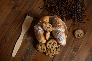 Breakfast capuccino, croissant and delicious cookies on a wooden table.