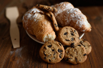 Breakfast capuccino, croissant and delicious cookies on a wooden table.