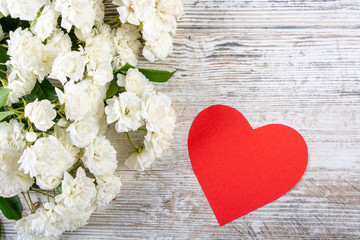 A bouquet of white roses and a paper heart for your text lie on a white texture board. Background for Valentine's day, wedding, love. Space for text, top view, copy space, flat lay.