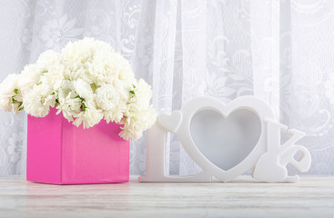 White roses in a pink square box and a white photo frame close-up. Valentine's day, wedding, declaration of love. Space for text, front view, copy space.