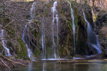 Waterfalls with a wooden bench in the lake. The Emerald Lake at Skra in Greece.