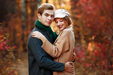 Fototapeta premium happy, couple in love hugs and smiles on the street, autumn, green scarf and cap, man and woman on a date, valentines day. walk in the park
