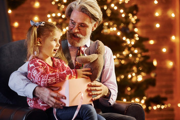 Cheerful fashioned senior man with grey hair and beard with little girl with gift box