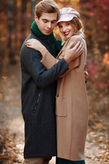 Fototapeta premium happy, couple in love hugs and smiles on the street, autumn, green scarf and cap, man and woman on a date, valentines day. walk in the park