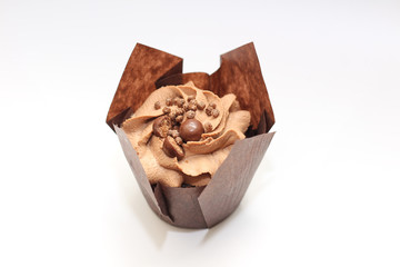 Isolated chocolate cupcake with cream top and crispy topping in paper on a white background