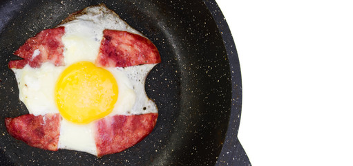Scrambled eggs with ham on a black frying pan in the shape of a cross. Isolated on a white background. Place for text on the right.