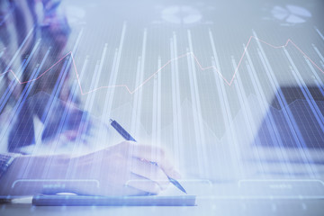 A woman hands writing information about stock market in notepad. Forex chart holograms in front. Concept of research. Double exposure