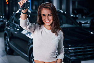 Fototapeta na wymiar Young woman in casual clothes standing near modern black car with keys in hands