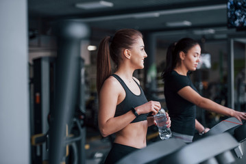 Two young girls in sportive clothes is in the gym together at treadmill