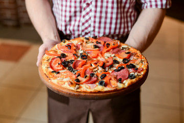 A waiter holds a plate of tasty food. Italian cuisine in restaurant, Delicious pizza with spinach, olives and mushrooms