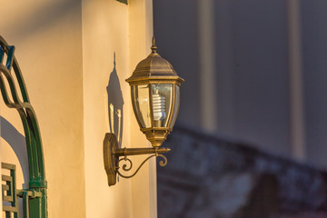 Fototapeta na wymiar Lamp post made of bronze with energy economy light bulb on the street wall