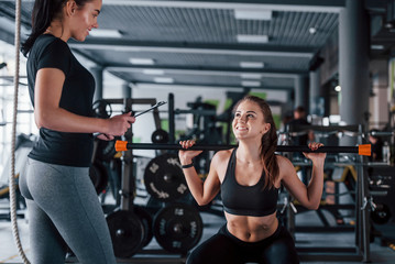 Fototapeta na wymiar Female personal trainer helping woman doing exercises in the gym