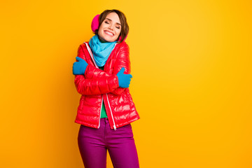 Photo of amazing lady enjoy warm coat in cold frosty weather hug herself wear stylish casual short red overcoat blue scarf gloves earmuffs pants isolated yellow color background