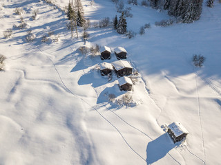 Aerial view of snow covered cottages in wild rural countryside. Tranquil scene with beautiful wooden houses in remote mountain area.
