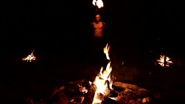 Man lays on ground two burning torches in dark. Low key, fire show. Long shot