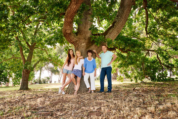 Fototapeta premium Family of four standing at base of large leafy tree