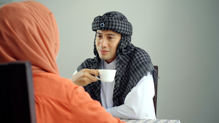 Young beautiful Asian Muslim man and women enjoying a relaxing moment in the coffee shop on a bright sunny day using mobile phone, smartwatch for mobile payment and QR code scan