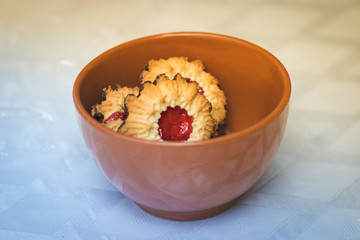 Crispy dough cookies stuffed with strawberry jam, with a chocolate-coated bottom. Inside a red pottery bowl. Against a blurry white background.
