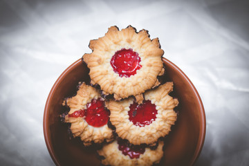 Crispy dough cookies stuffed with strawberry jam, with a chocolate-coated bottom. Inside a red pottery bowl. Against a blurry white background.