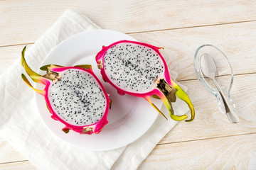 Ripe dragon fruit or pitaya cut in half in a white plate and spoon on a wooden table. Healthy vegetarian rich in B vitamins and tannin. Ready to eat.