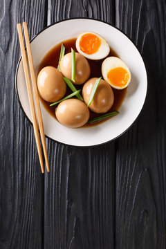 Nitamago eggs in soya marinade with green onions close-up in a plate. Vertical top view