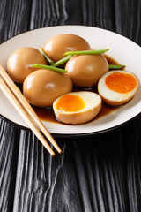 Nitamago eggs in soya marinade with green onions close-up in a plate. vertical