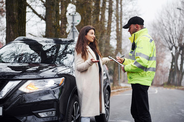 Male police officer in green uniform talking with female owner of the car on the road