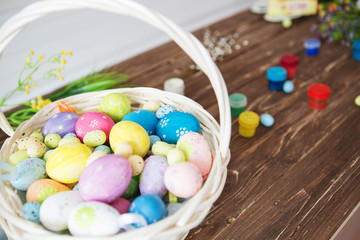 Close up painted Easter eggs in a basket and paintbrush resting on wood plank table.