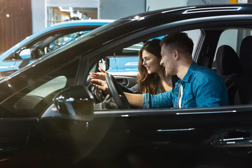 young woman manager in business suit consulting young man customer in electric car dealership center, professional cooperation