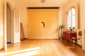 Photography studio setup with beige background and a mannequin. Beautiful decor and bright interior, wooden floor, modernist windows and doors, classic red sideboard