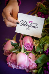 Elegant hand presenting a valentines card on a beautiful floral bouquet