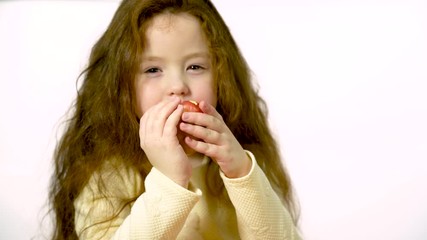 Girl 5-6 years old with long hair happily eats an apple in the studio on a white background